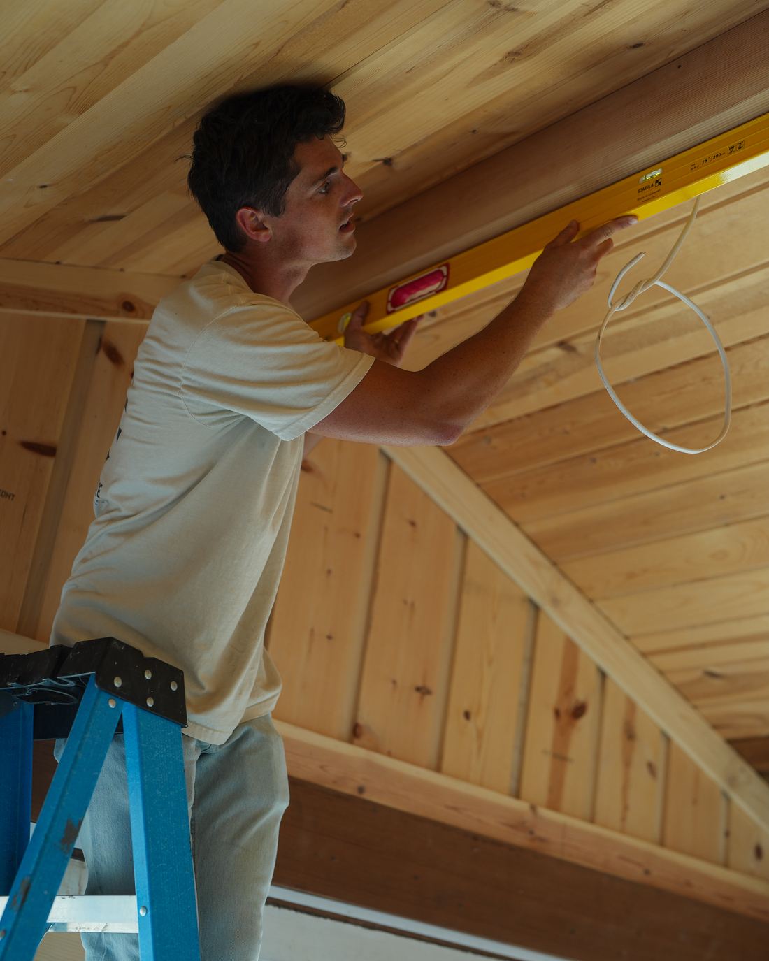 Checking a ceiling beam for level from a step ladder