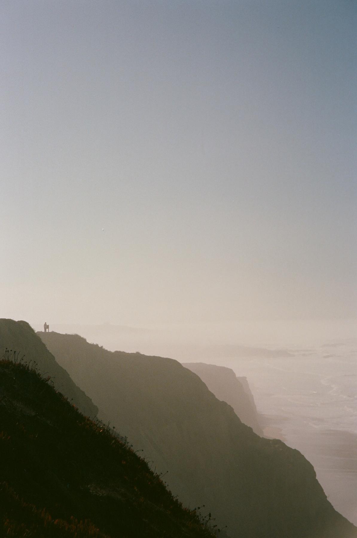 Two people standing on a bluff above the ocean in morning haze