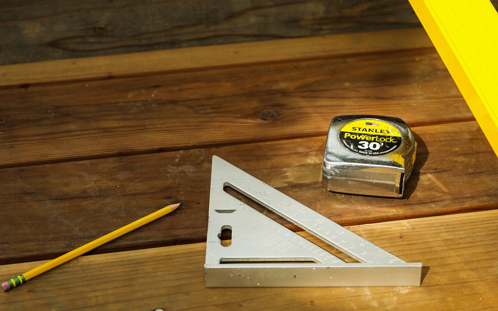 A level, speed square, tape measure and pencil laid out on redwood steps